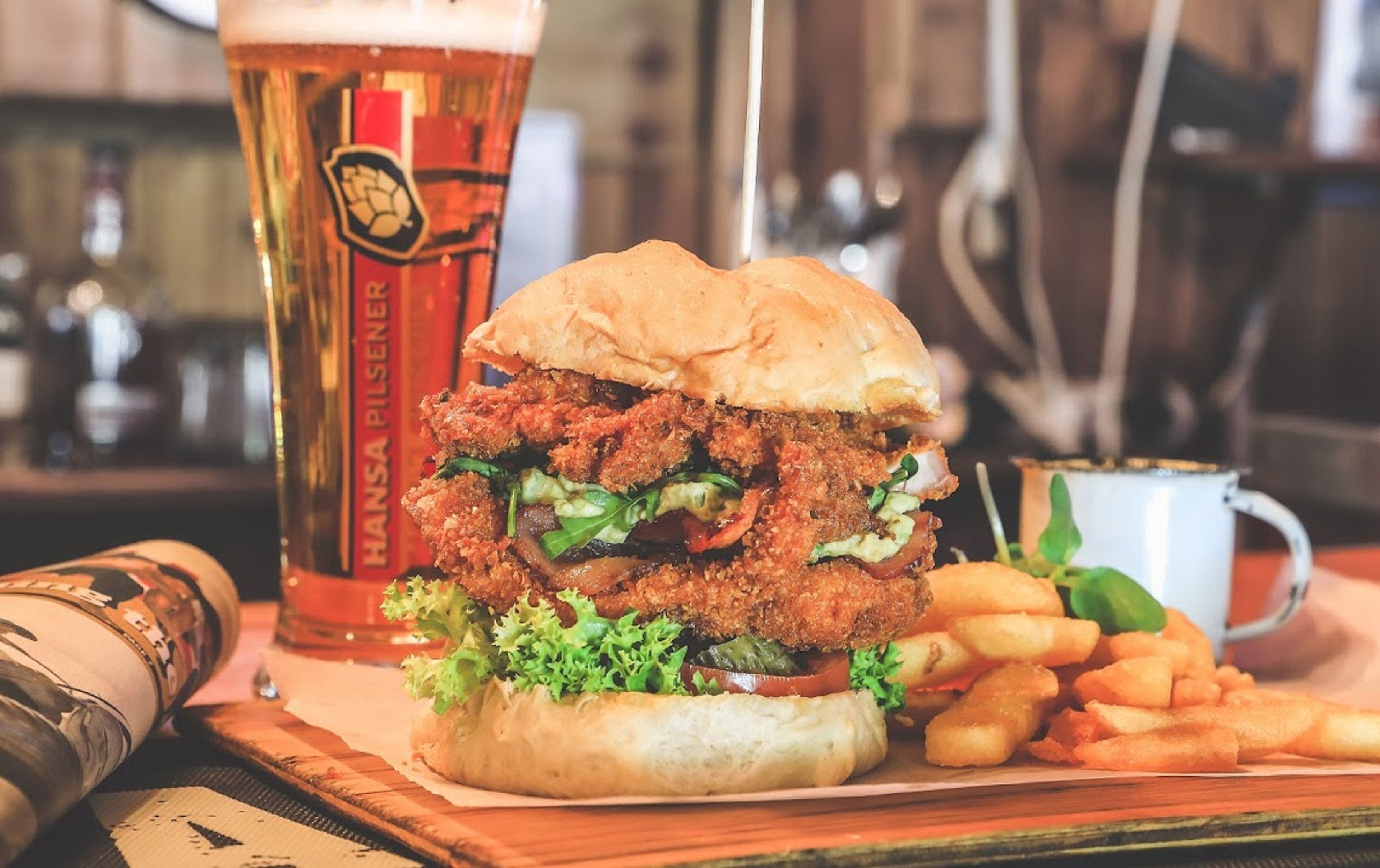 A burger with fries and a beer mug on a wooden table.