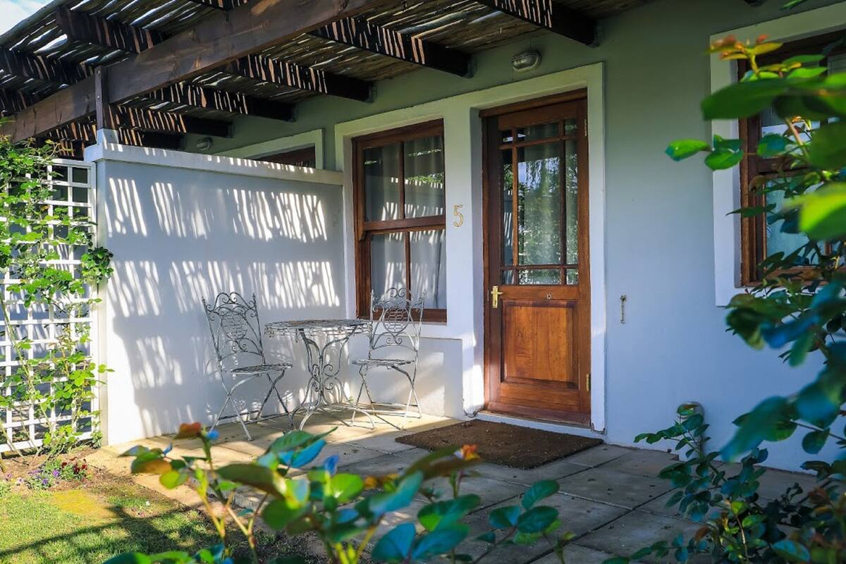 A house with a wooden door, a number '5' on the wall, and a patio with a table and chairs.