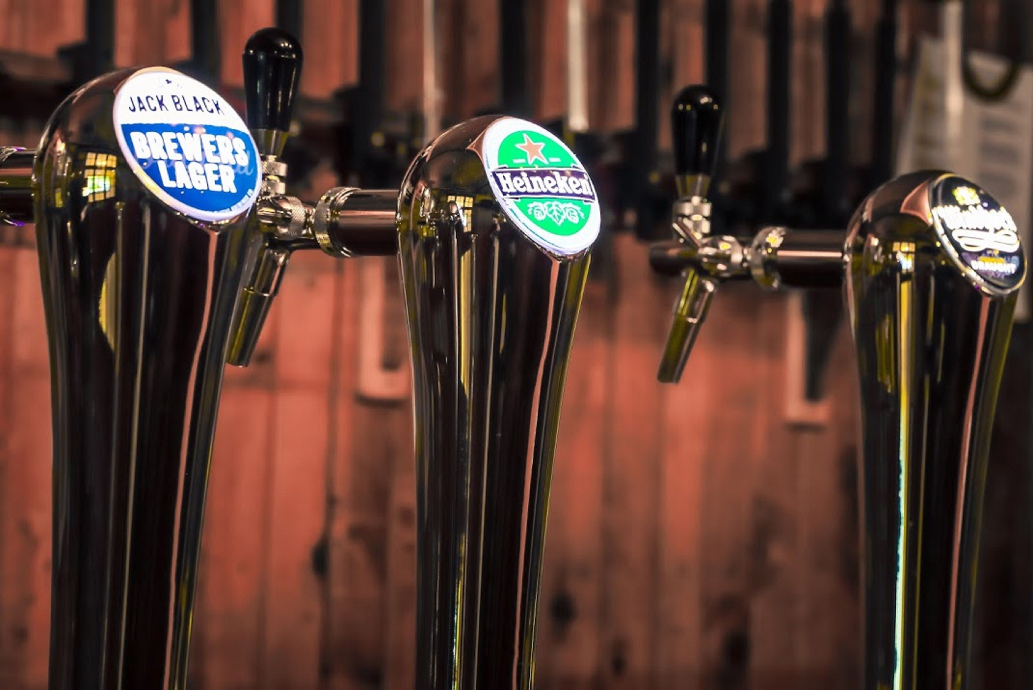 Une rangée de robinets à bière avec des étiquettes indiquant les marques Jack Black, Brewers Lager et Heineken.
