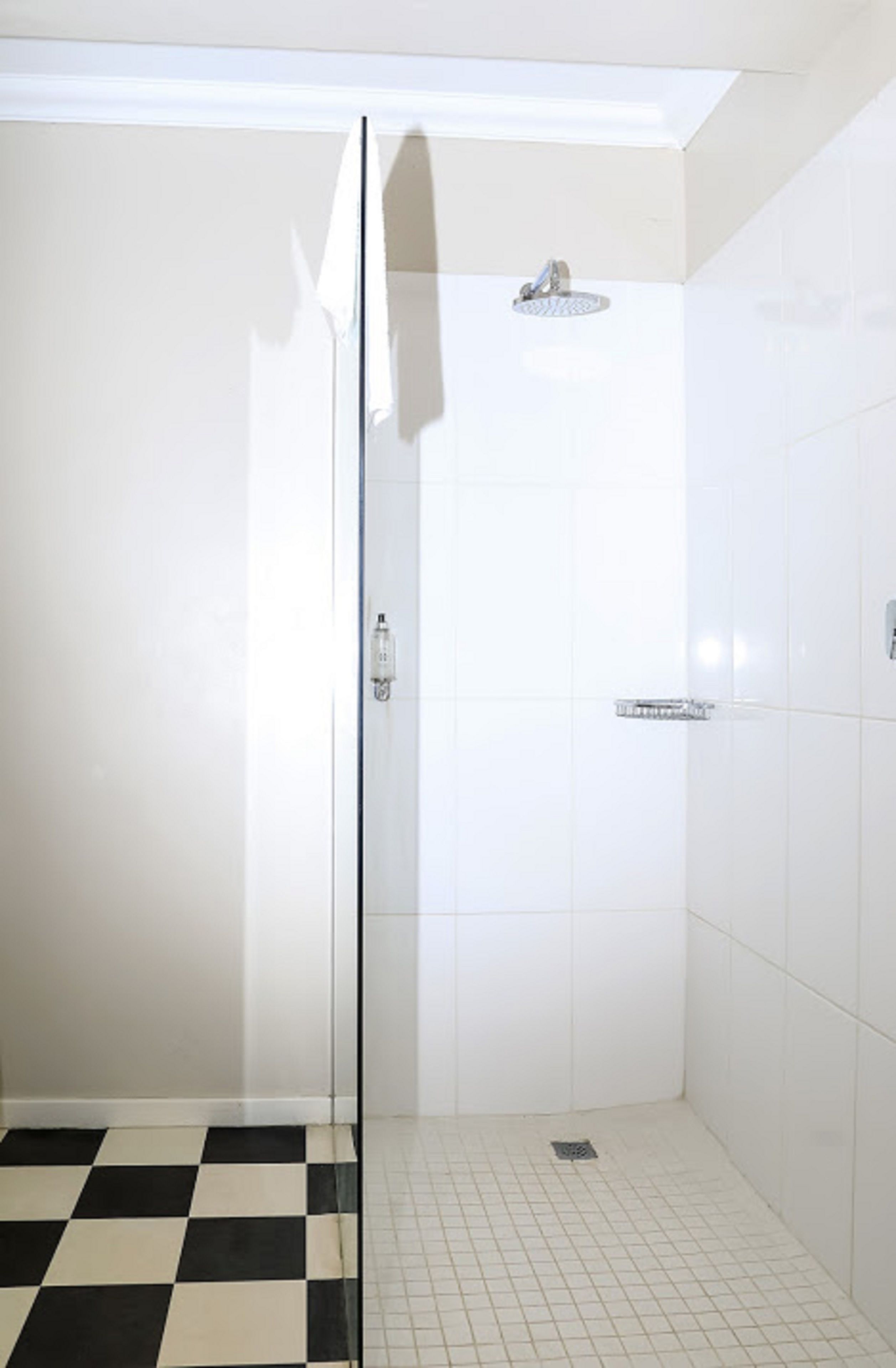 A bathroom with a glass shower door, white tiled walls, and a checkered floor.