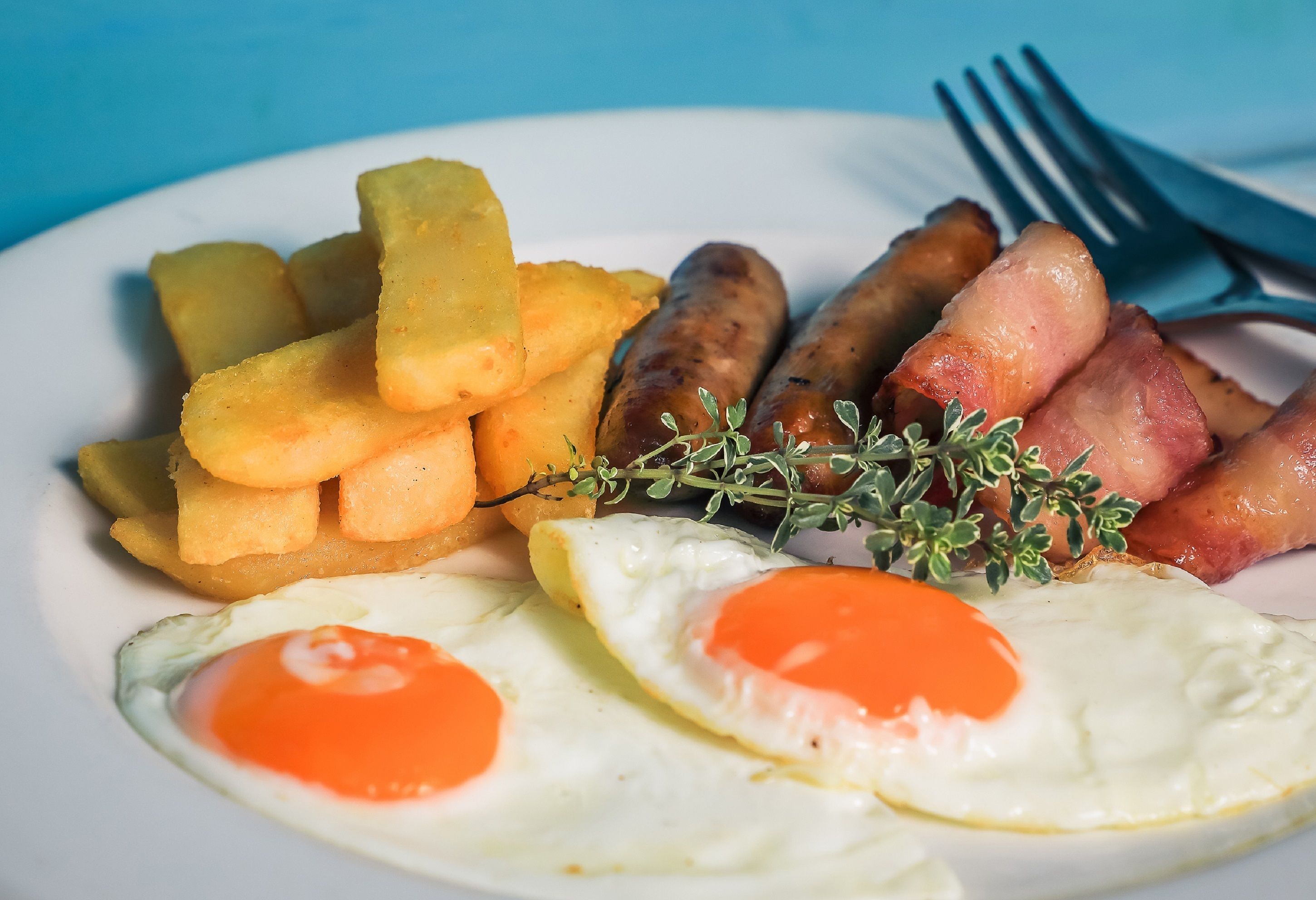 A plate with fried eggs, sausages, and potato wedges.