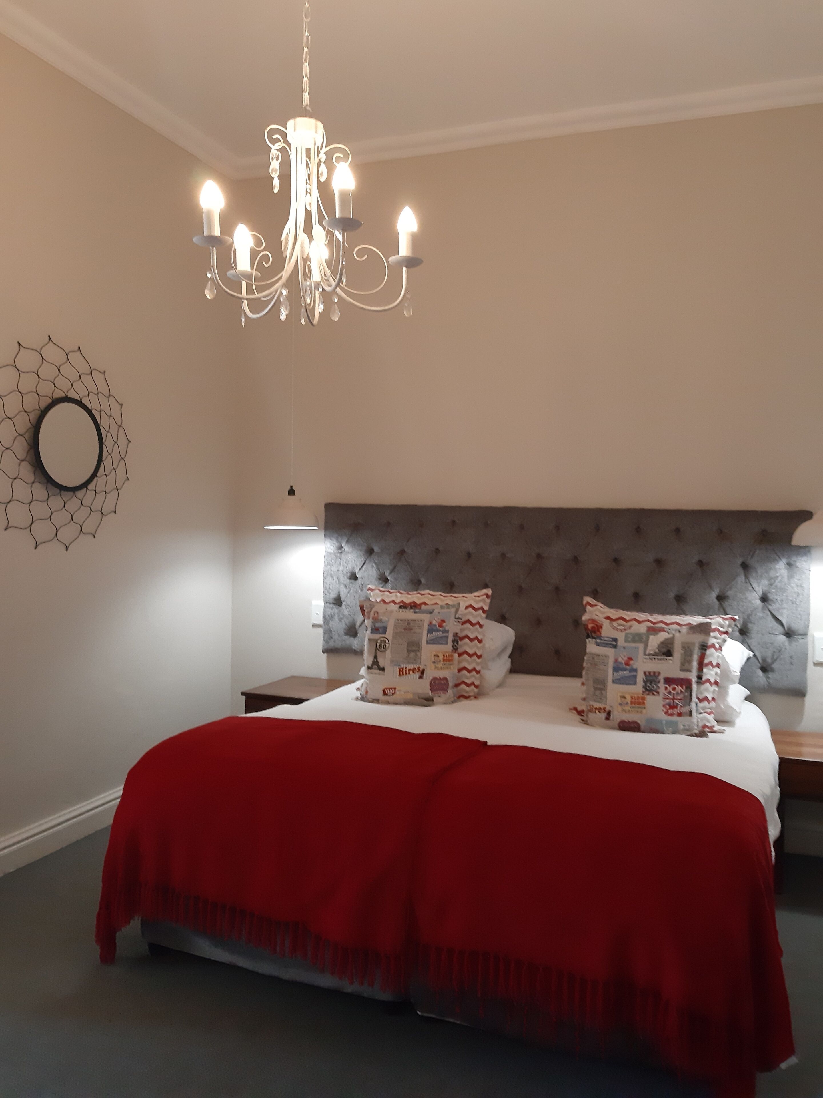 Une chambre à coucher avec une tête de lit capitonnée, un lustre, une couvre-lit rouge et des coussins décoratifs.