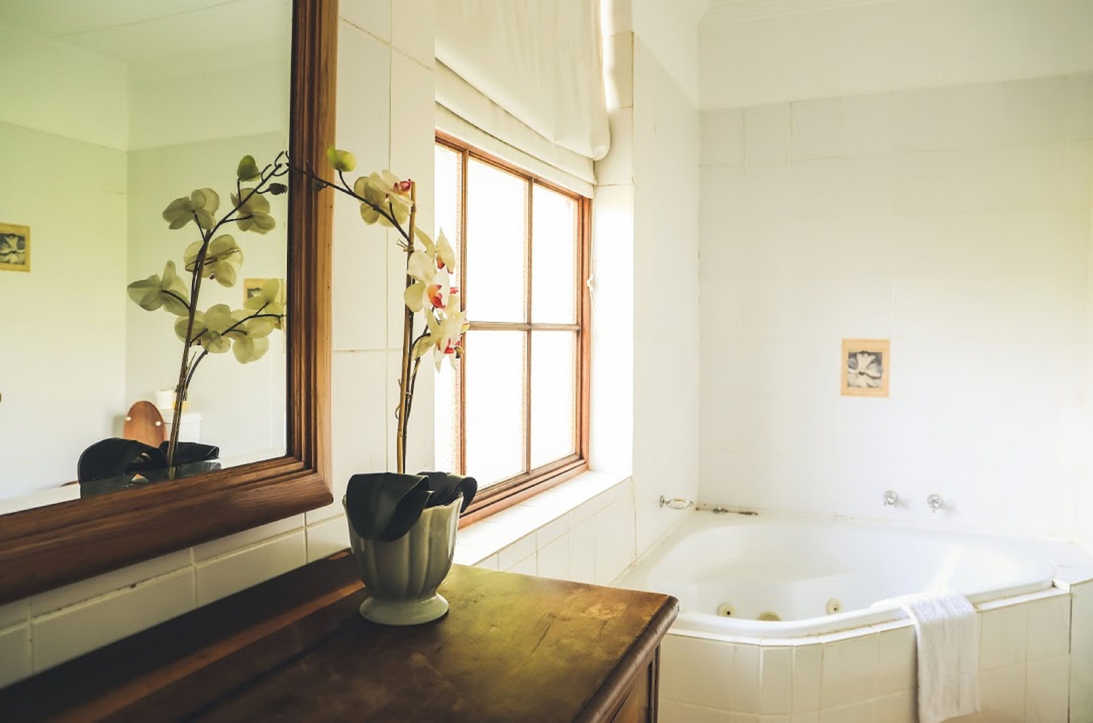 Une salle de bain avec un grand miroir, une baignoire et une fenêtre avec des rideaux.
