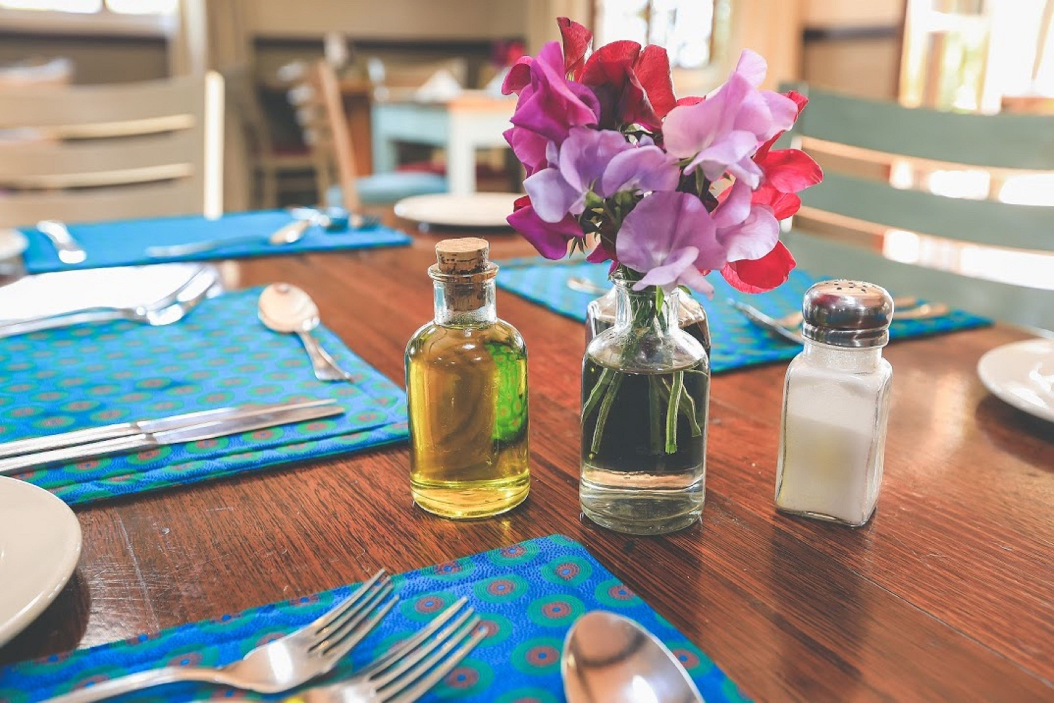 A dining table set with a blue tablecloth, two bottles of oil, a salt shaker, and a vase with purple flowers.