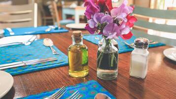A dining table set with a blue tablecloth, two bottles of oil, a salt shaker, and a vase with purple flowers.
