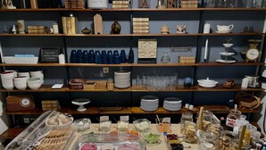 Disposição de buffet com diversos alimentos, além de seleção de copos e louças em prateleiras.