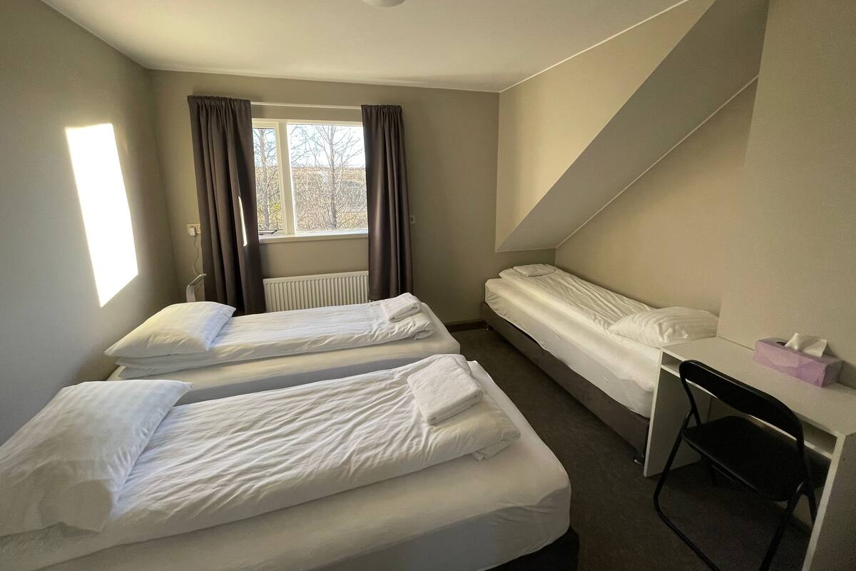 Una habitación con dos camas, un escritorio y una ventana con cortinas.