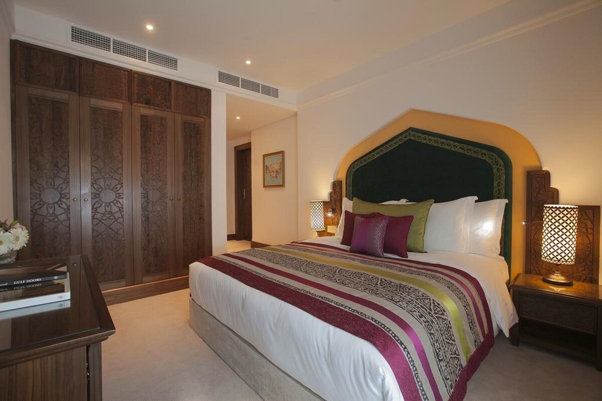 Una habitación de hotel con una cama grande, un armario, un escritorio con lámpara y un cuadro en la pared.