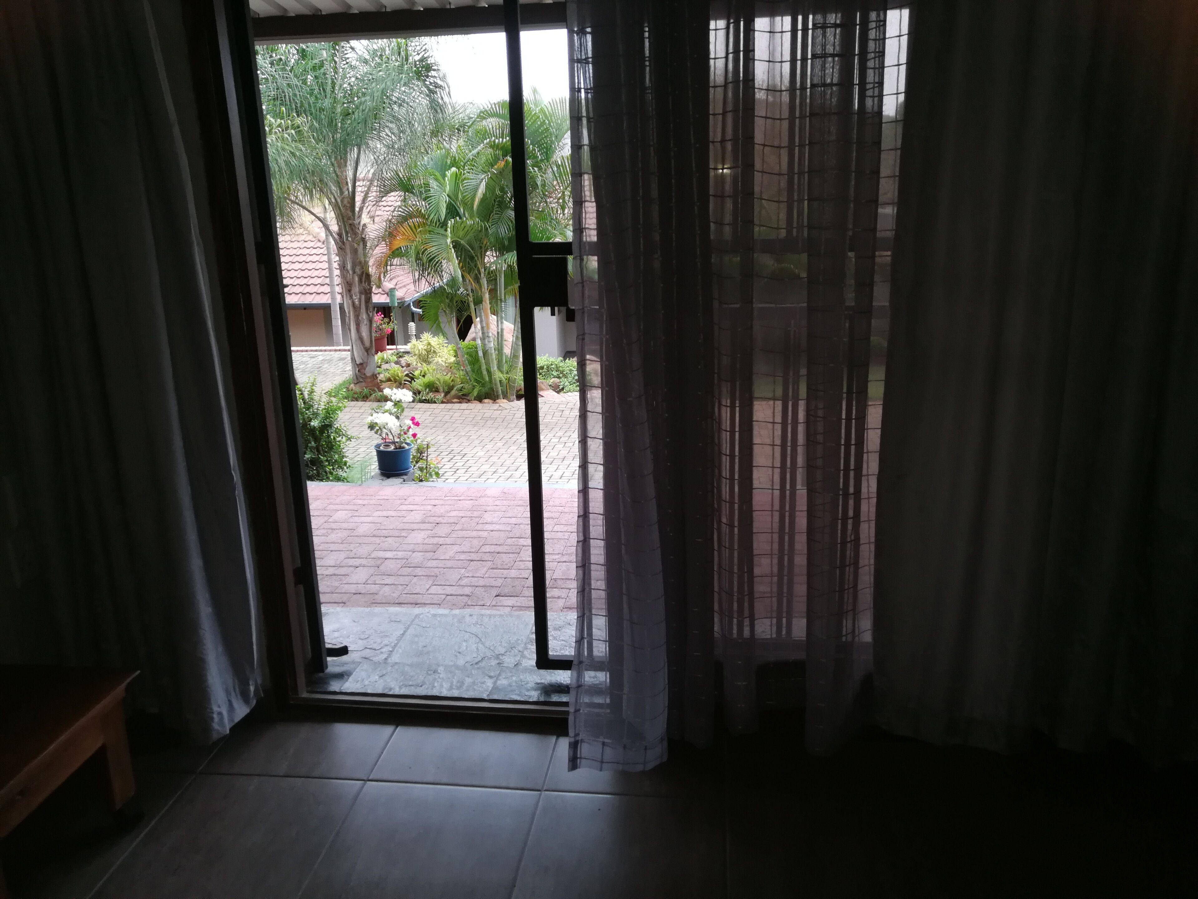 Una habitación con puerta de vidrio corredera que da a un patio con plantas en macetas y suelo de baldosas.