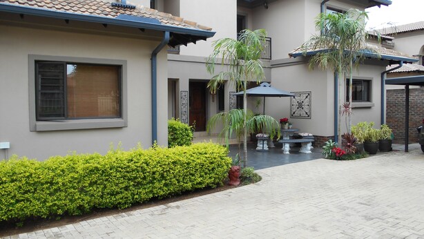 A modern house with a paved courtyard, a covered patio area, and a variety of potted plants. - Meerkat Manor (Nkomazi)