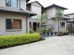 A modern house with a paved courtyard, a covered patio area, and a variety of potted plants. - Meerkat Manor (Nkomazi)