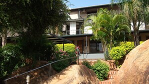 A courtyard with large rocks, a staircase, and a building with a balcony. - Meerkat Manor (Nkomazi)