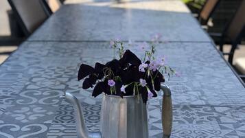 A metal pitcher with flowers on a patterned table in an outdoor setting.