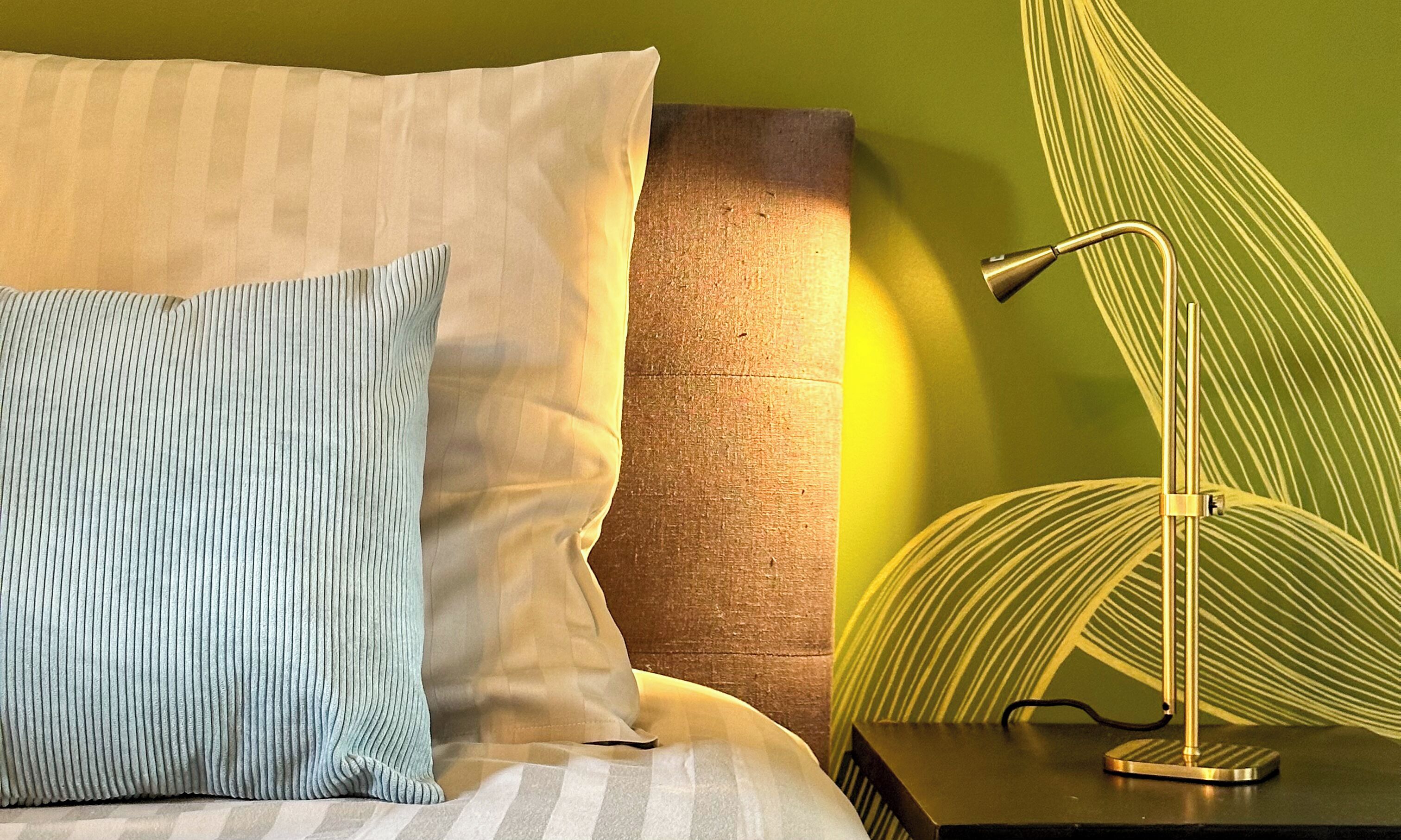 A neatly made bed with striped pillows, a bedside lamp, and a textured wall behind it.