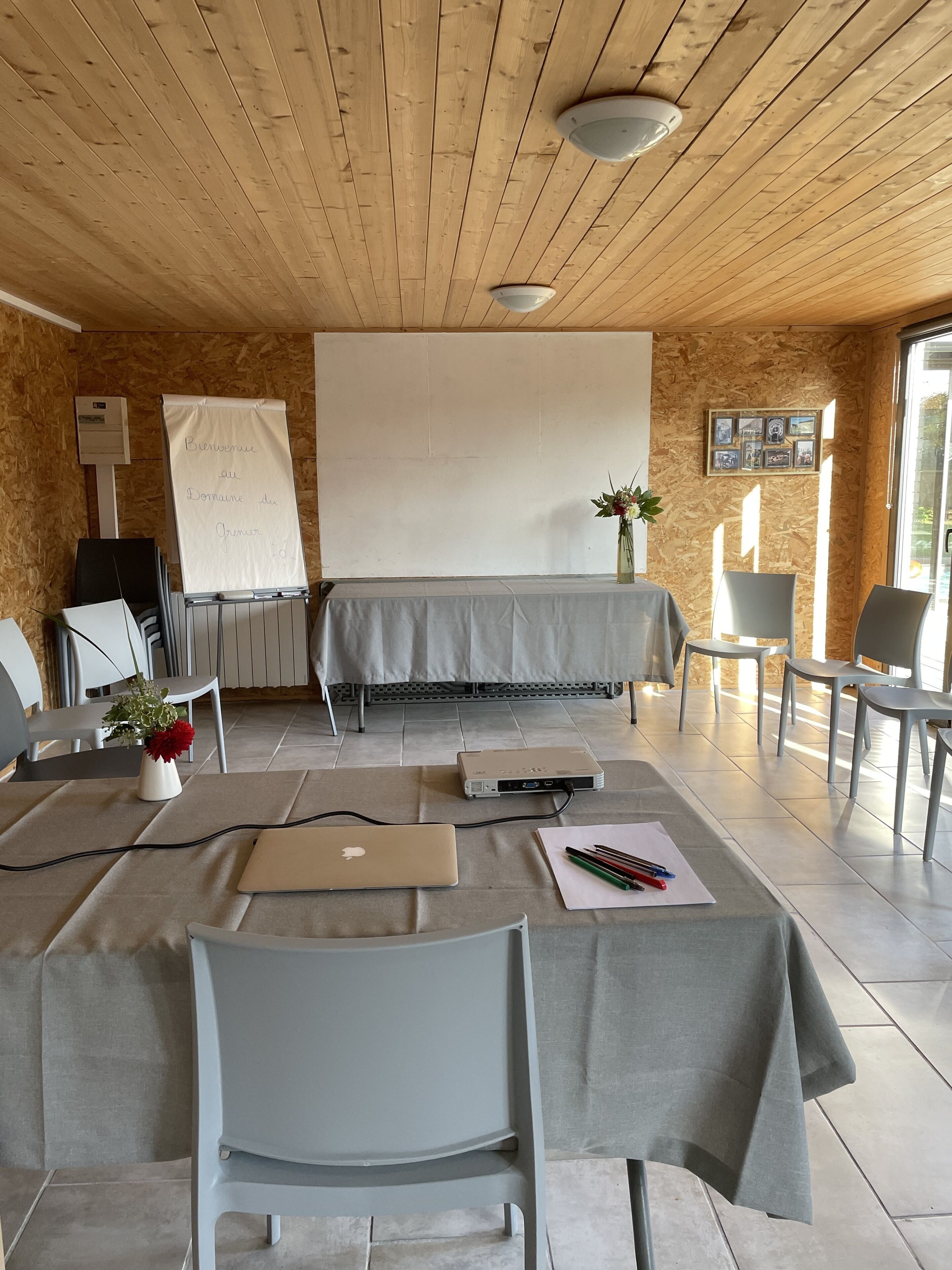 A conference room with a wooden ceiling, a whiteboard, a projector, a laptop, and a table with chairs.