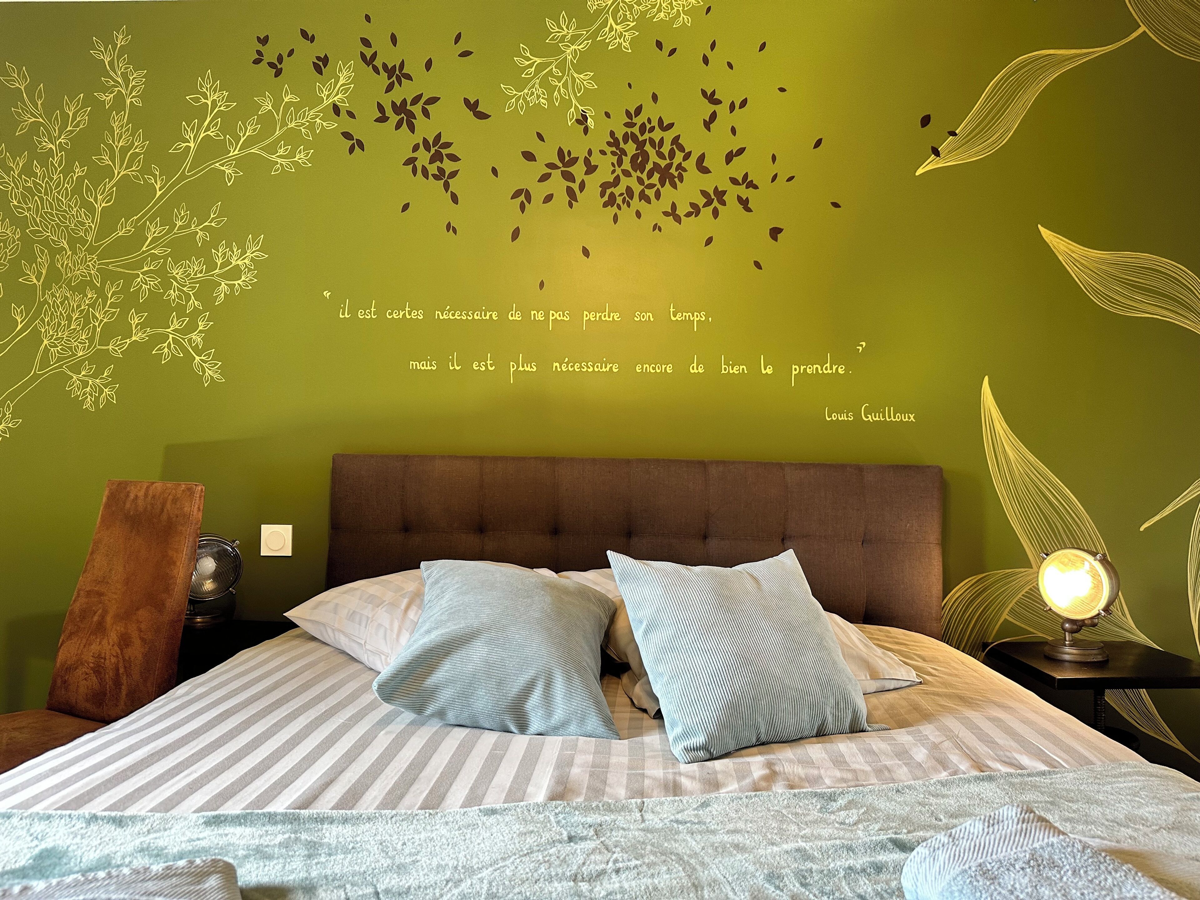 Un dormitorio con pared verde, cama con ropa de cama a rayas y una cita decorativa de Louis Guillaum.