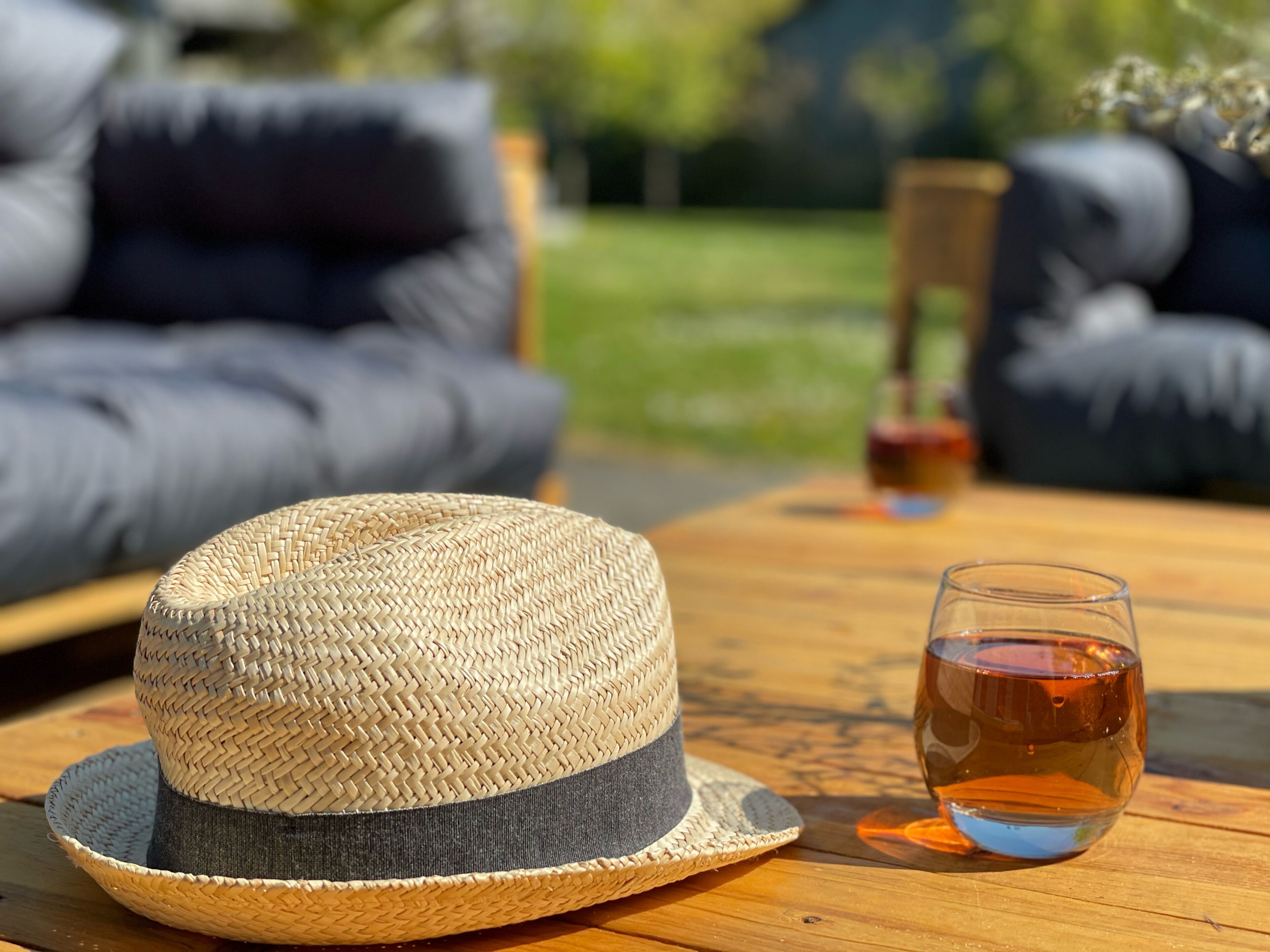 A straw hat on a wooden table with a glass of amber liquid.