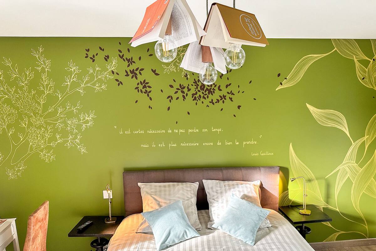 A bedroom with a green wall, a bed with striped bedding, and a quote in French.