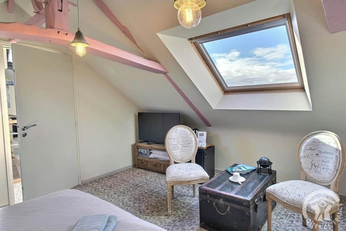 A bedroom with a sloped ceiling, a skylight, a bed, a desk with a chair, and a television.