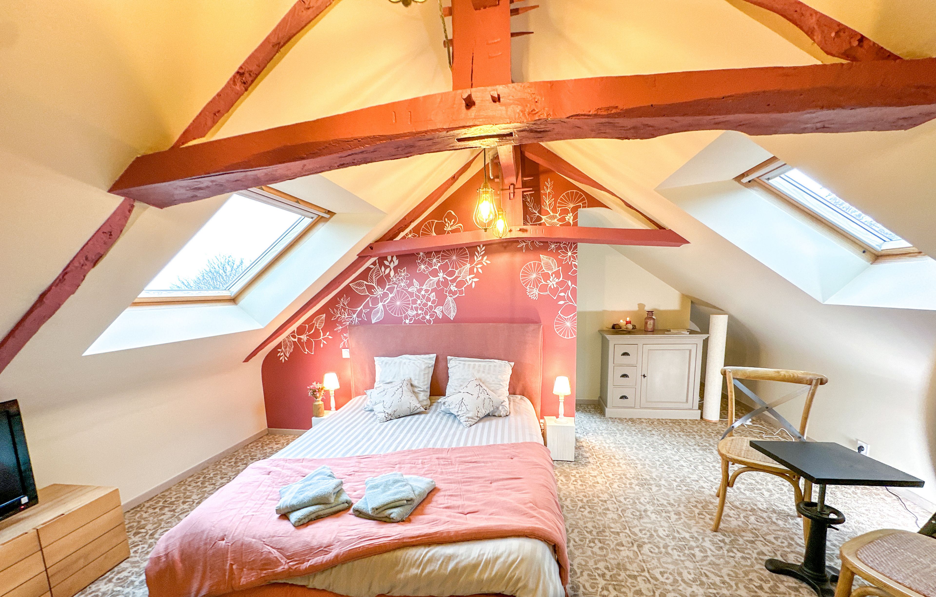 A bedroom with a sloped ceiling, a bed with pink bedding, a nightstand, a dresser, a chair, and a small table.