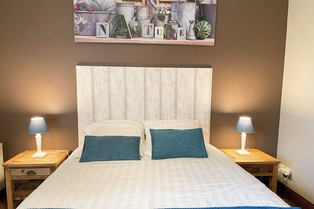 Ein ordentlich bezogenes Bett mit zwei Kissen, einer blauen Decke und zwei Nachttischlampen auf Holznachttischen.