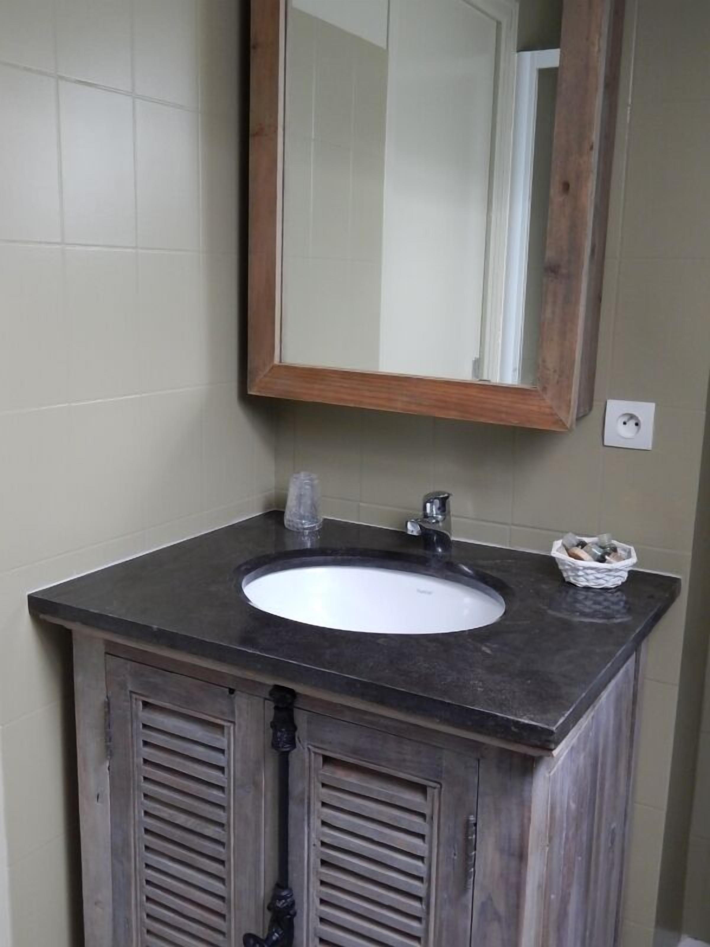 Une salle de bain avec un lavabo au comptoir de couleur sombre, un miroir et des armoires en bois.