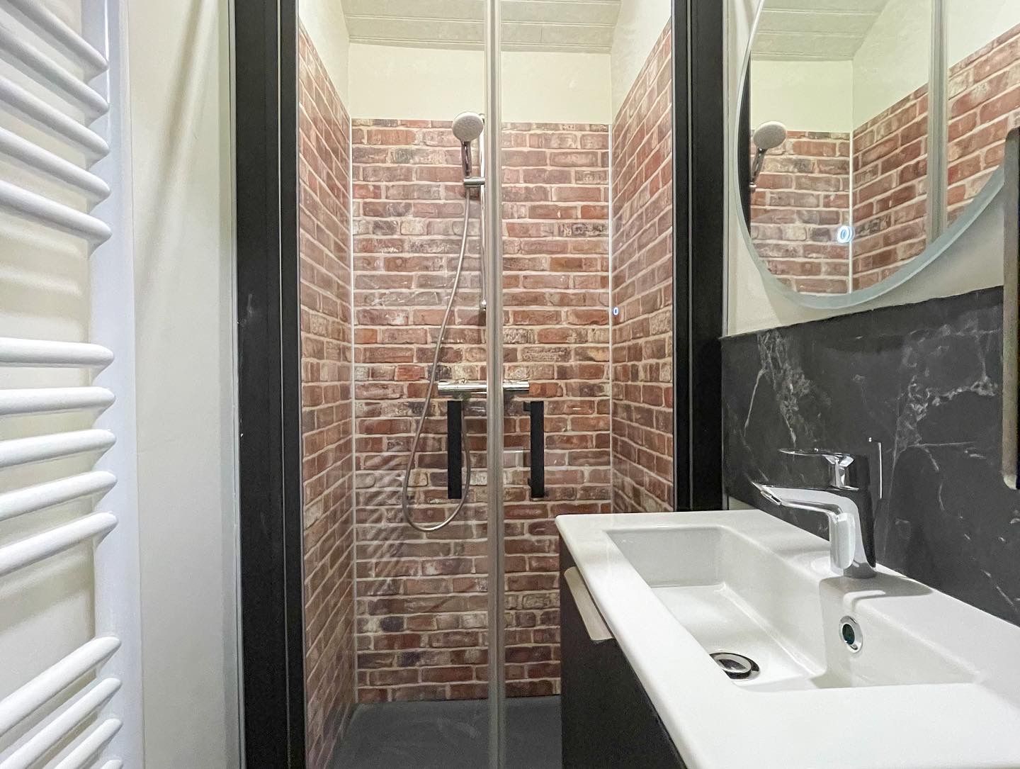 Un baño con cabina de ducha de vidrio, lavamanos blanco y espejo.