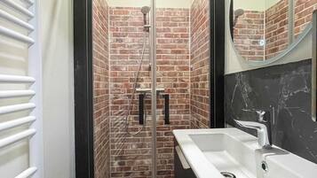 Un baño con cabina de ducha de vidrio, lavamanos blanco y espejo.