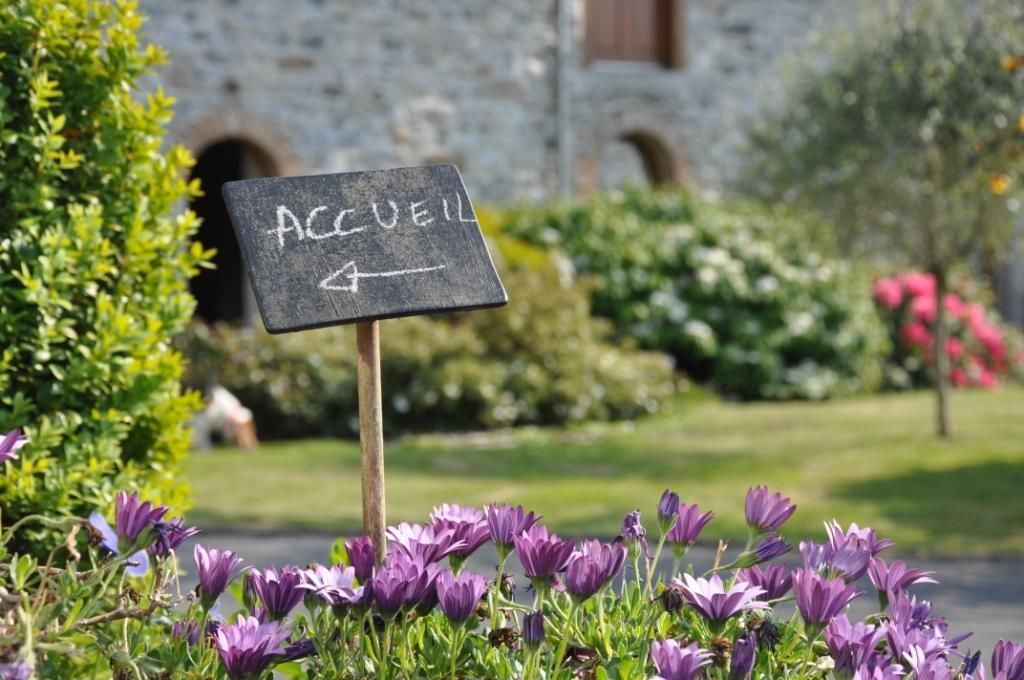 A sign with the word "ACCEIL" and an arrow pointing to the right, placed in front of a building with a stone facade and arched windows.