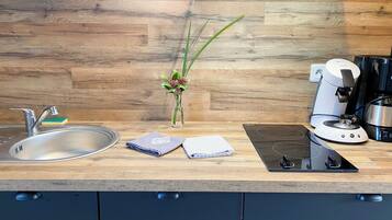 A modern kitchen with a wooden backsplash, stainless steel sink, a coffee maker, and a small vase with green plants.