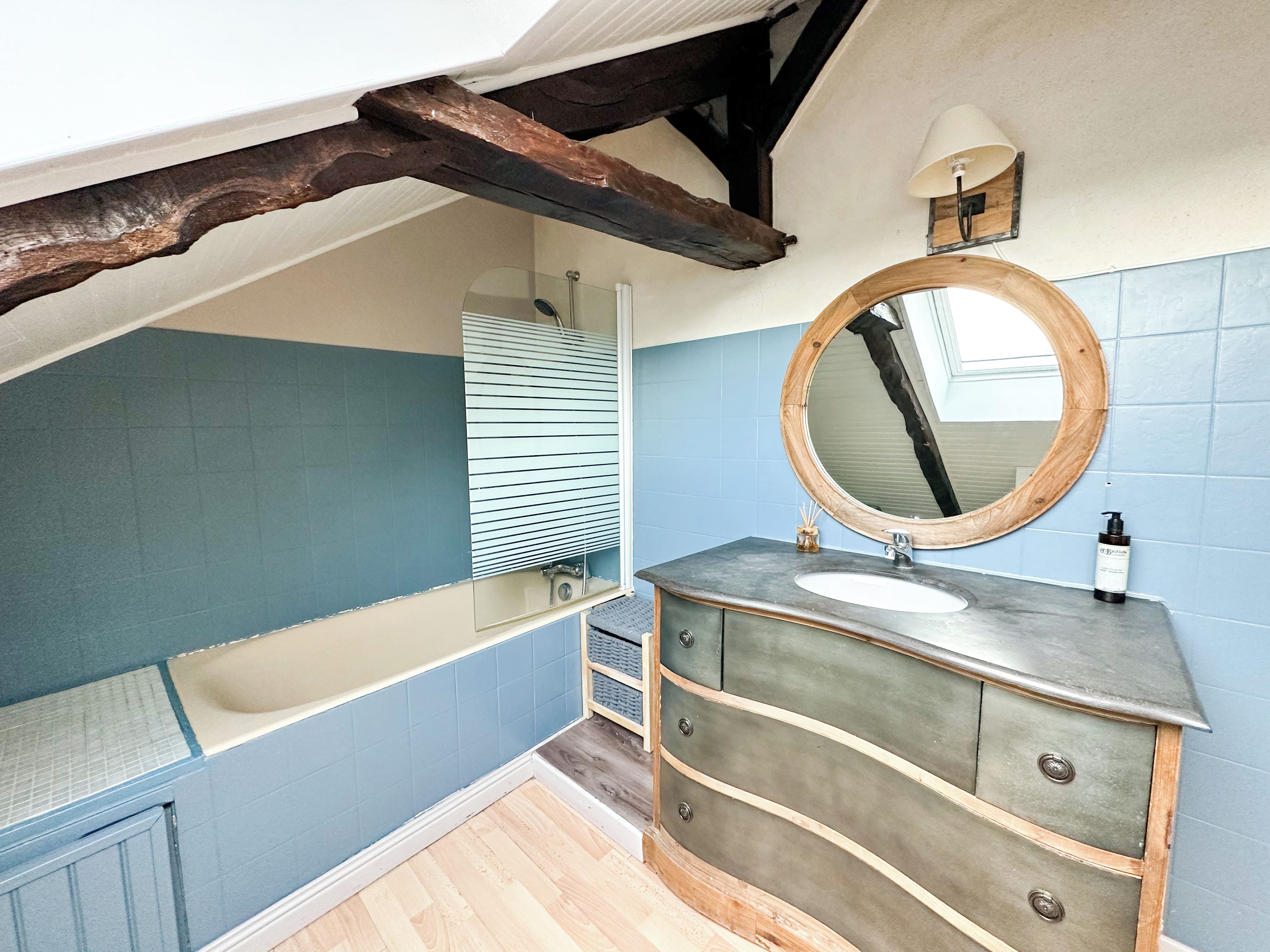 A bathroom with a bathtub, a vanity with a mirror, and a wooden ceiling beam.