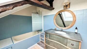 A bathroom with a bathtub, a vanity with a mirror, and a wooden ceiling beam.