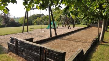 Kids can play on the swing set, slide, and climbing structure in this playground area surrounded by a fence and a grassy field.