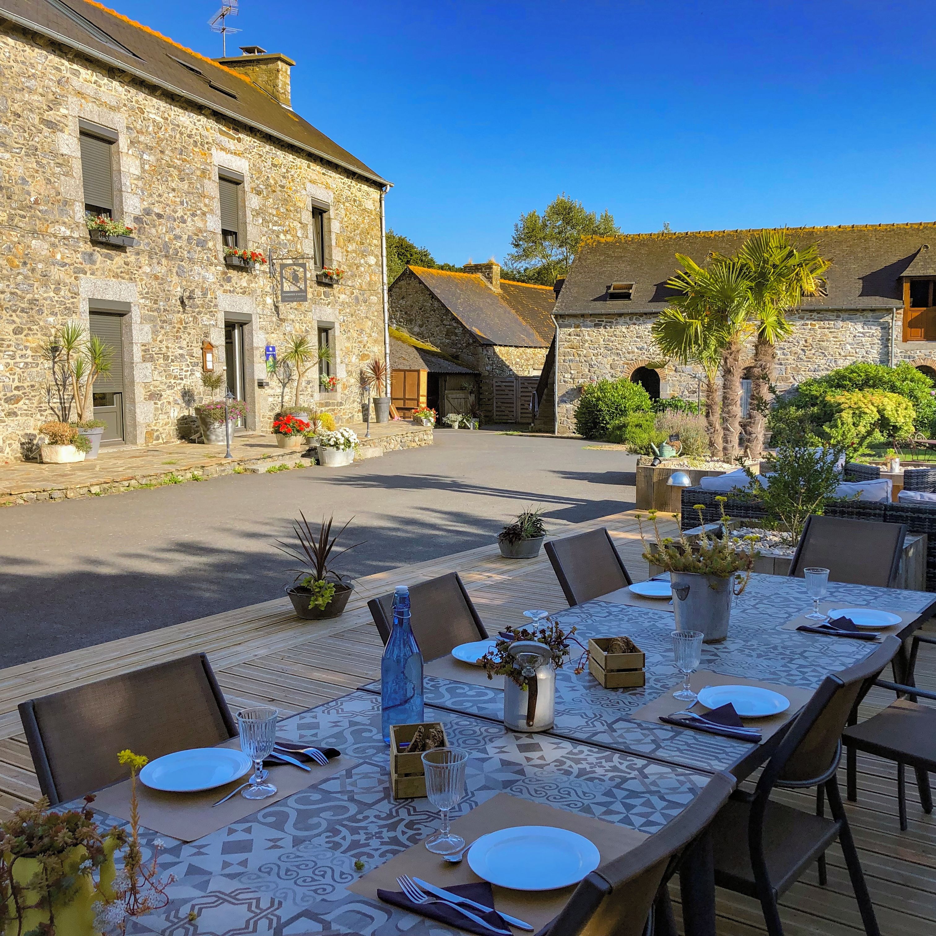 An outdoor dining area with stone buildings, tables set for two, and potted plants.