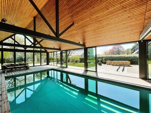 Un área de piscina interior moderna con techo de madera, ventanas amplias y vista al jardín.