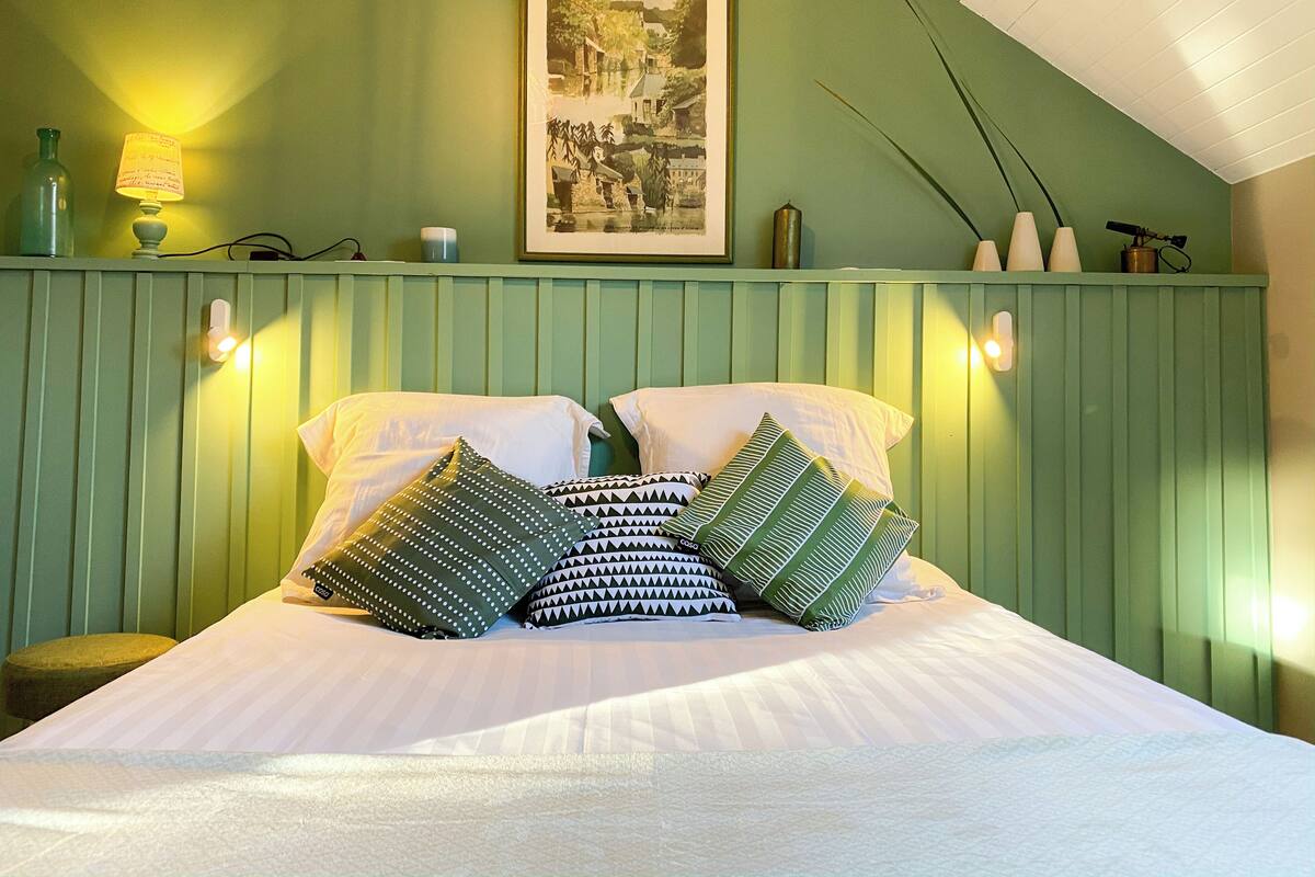Ein Bett mit weißer Bettwäsche und gemusterten Kissen, eine grüne Wand und ein gerahmtes Bild über dem Bett.