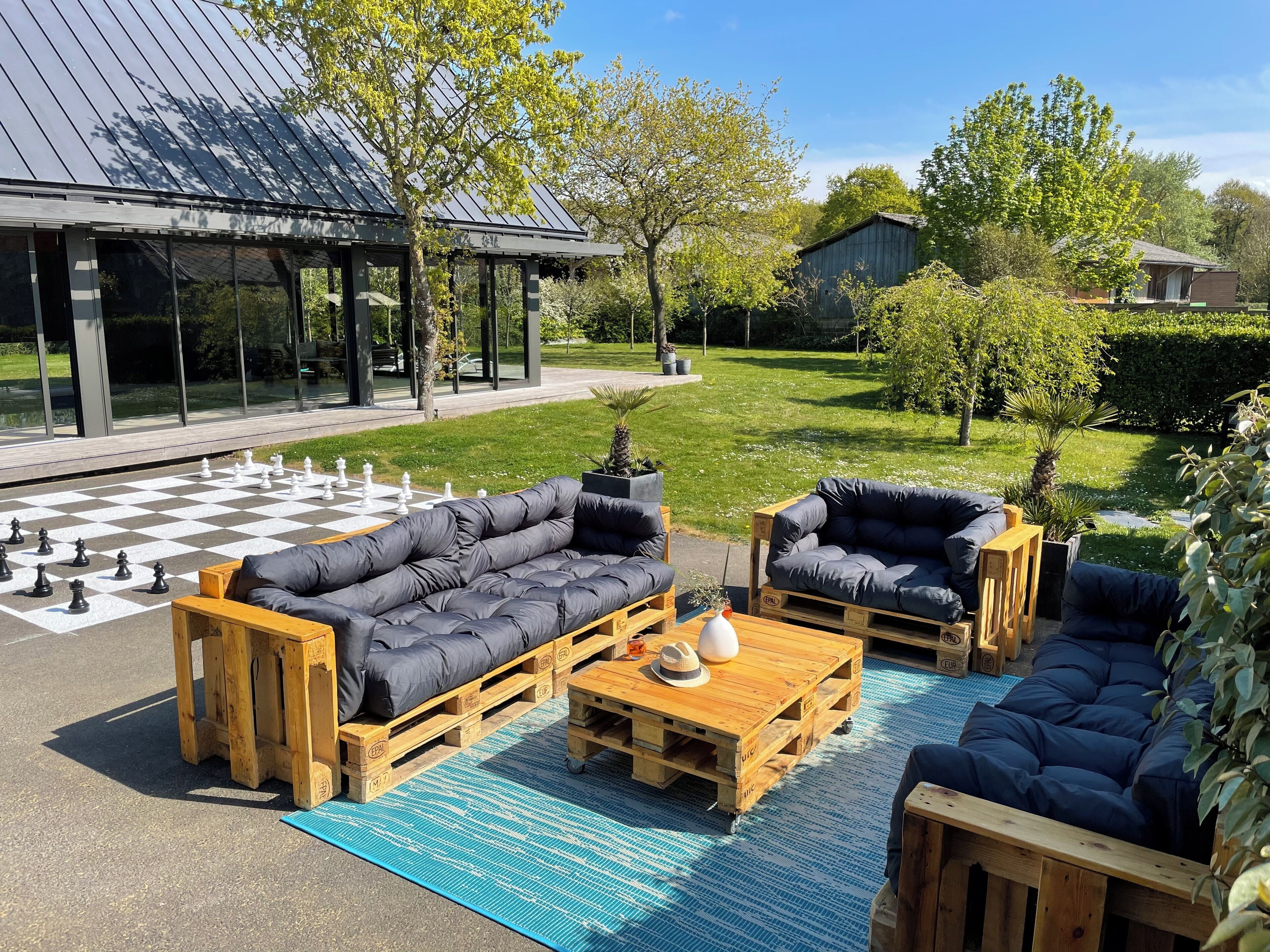 An outdoor seating area with a chessboard, wooden furniture, and a view of a building with a metal roof.