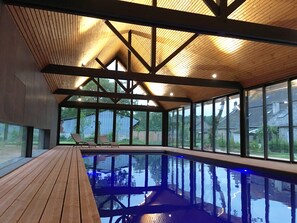 A modern indoor swimming pool with wooden beams and large windows. - Gîtes Domaine du Grenier (Yffiniac)