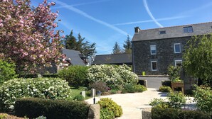 A stone building with a paved pathway leading to the entrance, surrounded by well-maintained gardens and flowering trees. - Gîtes Domaine du Grenier (Yffiniac)
