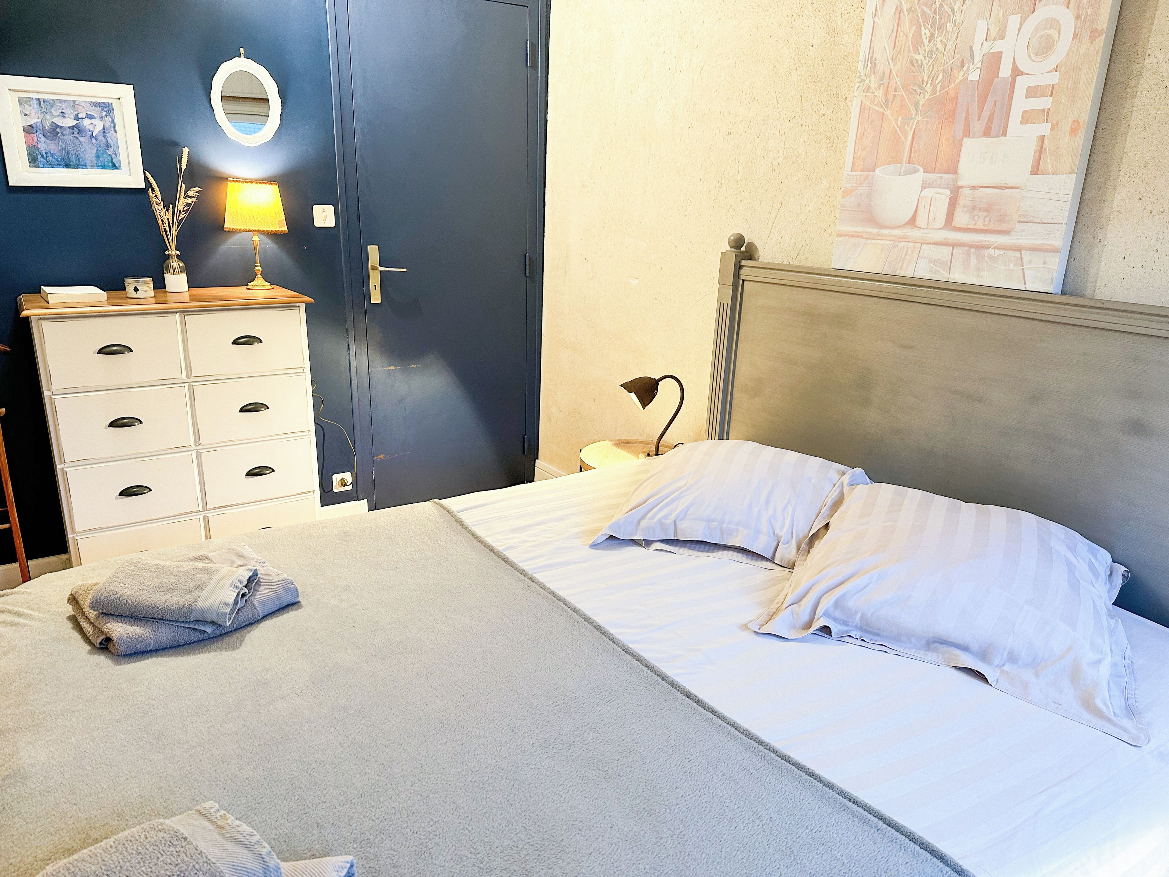 Une chambre à coucher avec un lit, une commode, une lampe et une affiche accrochée au mur.