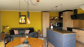 A modern kitchen with a central island, a dining area with a wooden table and chairs, and a living area with a sofa and a coffee table.