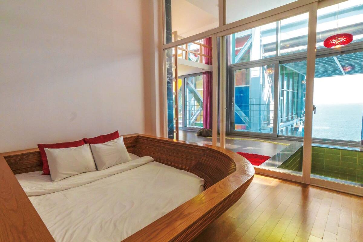 Une chambre moderne avec un lit en bois, de grandes fenêtres et une vue sur le pont d’un navire.