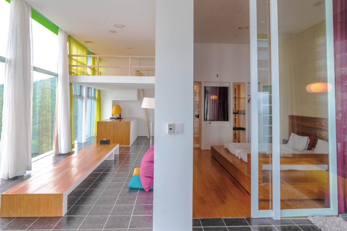 Une chambre d’hôtel moderne avec un grand lit, un bureau et un coin salon comprenant un banc et des coussins.