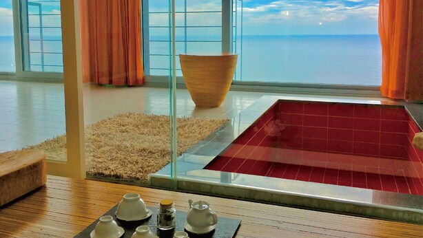 Een moderne kamer met een groot raam, een houten kom, een rode badkuip en een tafel met theepotten.