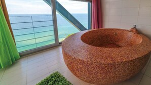 Une salle de bain moderne avec une baignoire en mosaïque, de grandes fenêtres donnant sur l’océan et un luminaire suspendu rouge.