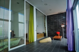 A modern bathroom with a glass shower enclosure, a wooden bench, and a floor lamp.