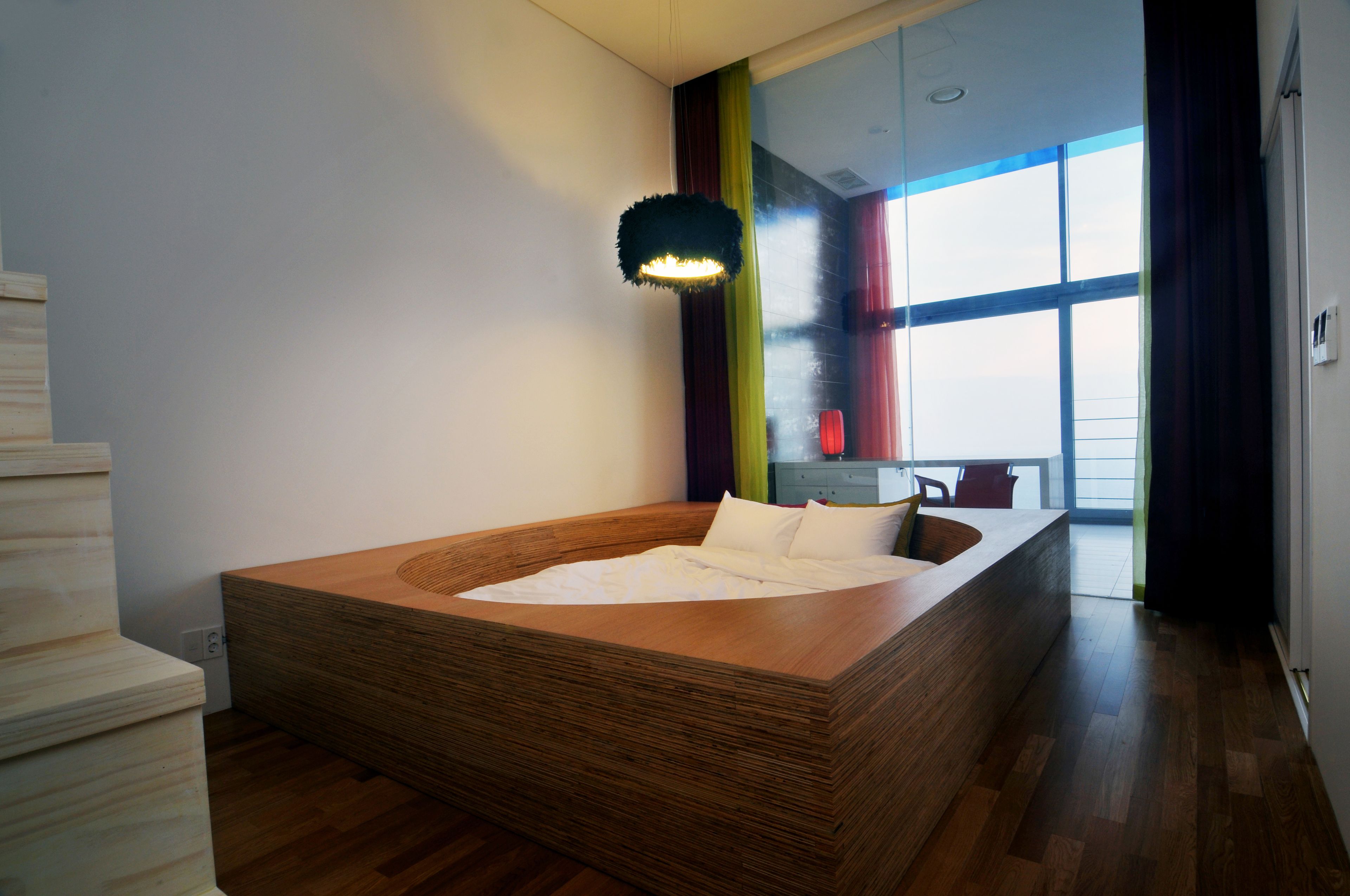 Une chambre moderne avec un lit en bois, une grande fenêtre et un escalier.