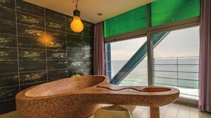 Een moderne badkamer met een uniek mozaïekbad, een hanglamp en uitzicht op de oceaan door grote ramen.
