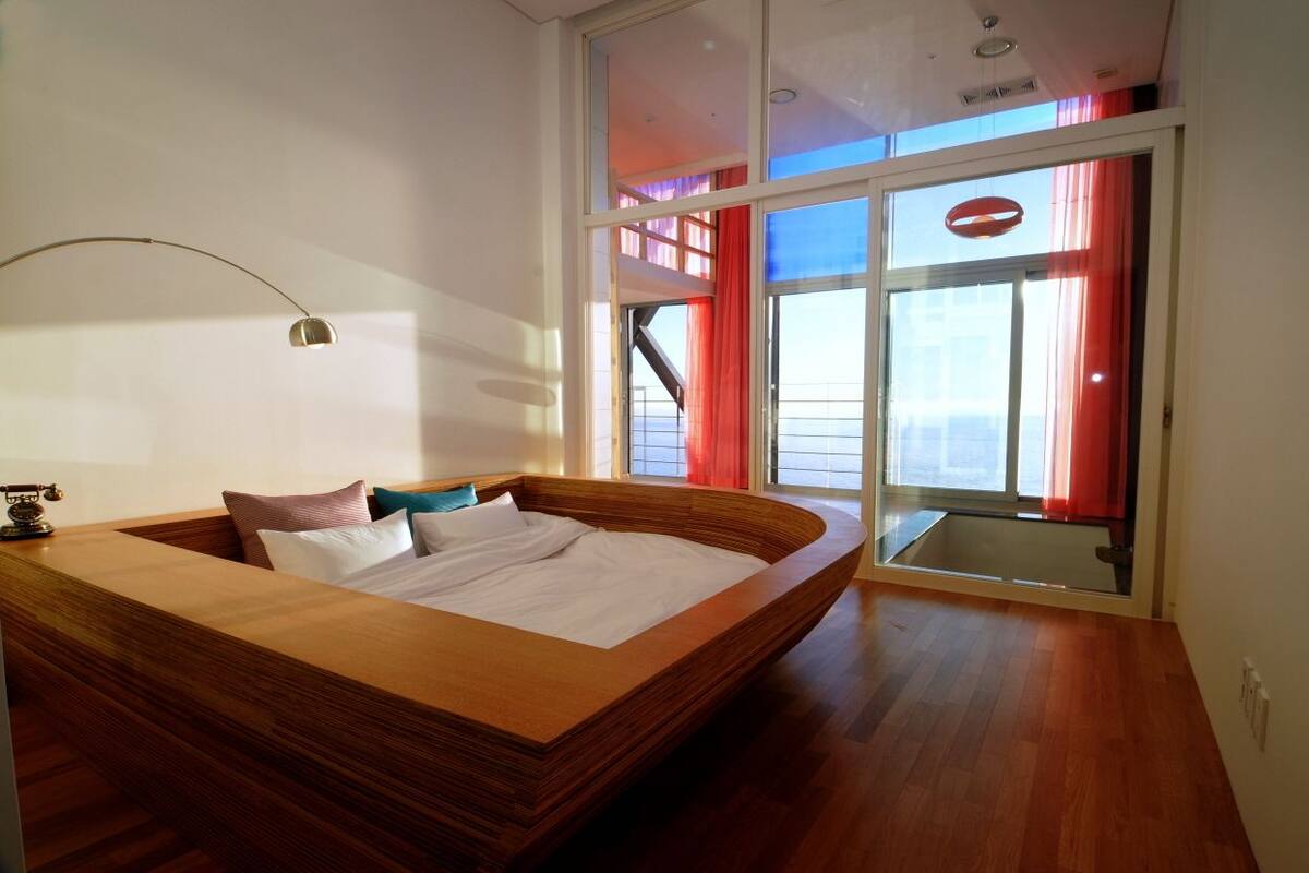 Une chambre moderne avec un lit en bois, une grande fenêtre et une vue sur le ciel.