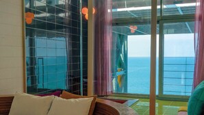 Een moderne kamer met een gebogen houten bed, een glazen wand en uitzicht op zee.